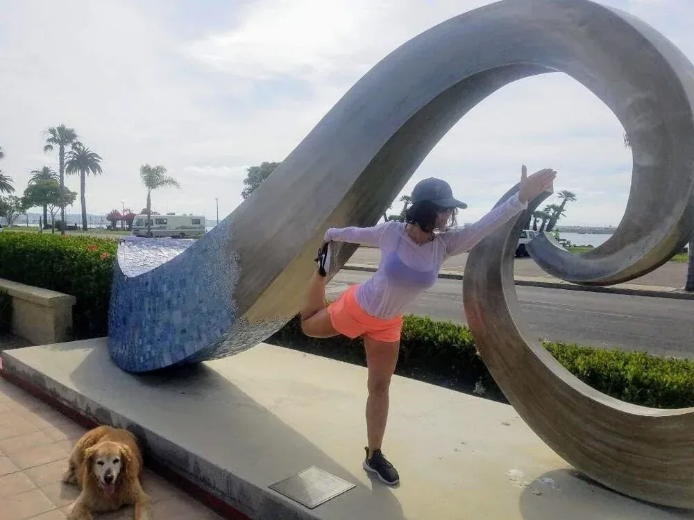 A person stretching by the Sunset Cliffs sculpture in Ocean Beach with a dog nearby